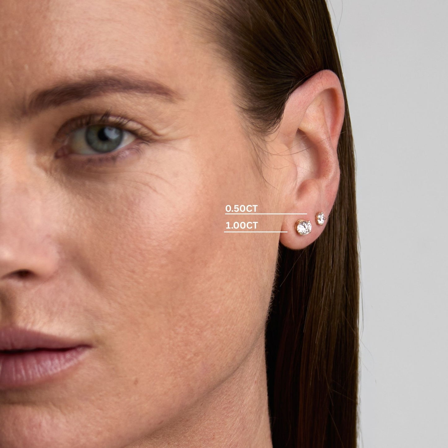 Woman wearing round lab grown diamond stud earrings in 0.50ct and 1.00ct sizes