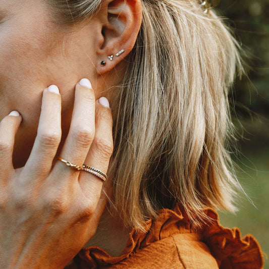 Woman wearing natural diamond stud earrings in yellow gold with stacked ear piercings
